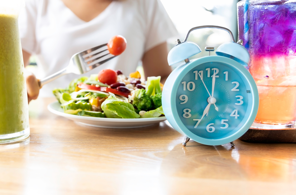 Selective focus of blue clock which woman make a Intermittent fasting with  a Healthy food of salad .Healthy lifestyle Concept.