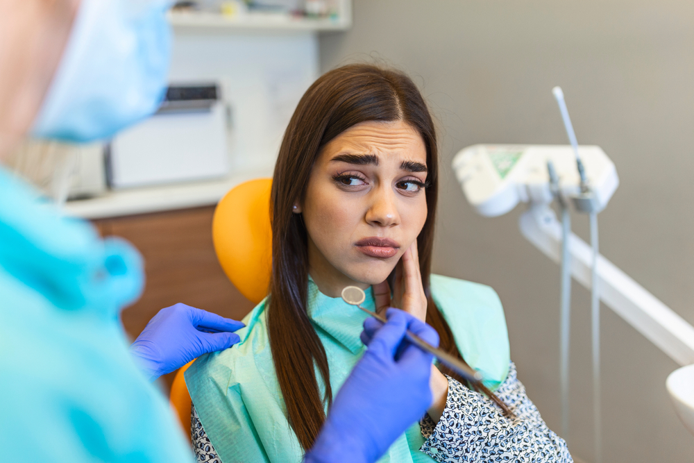 Young woman holding cheek in chair at dentist, having toothache. Shot of a young woman suffering from toothache while sitting in the dentist's chair