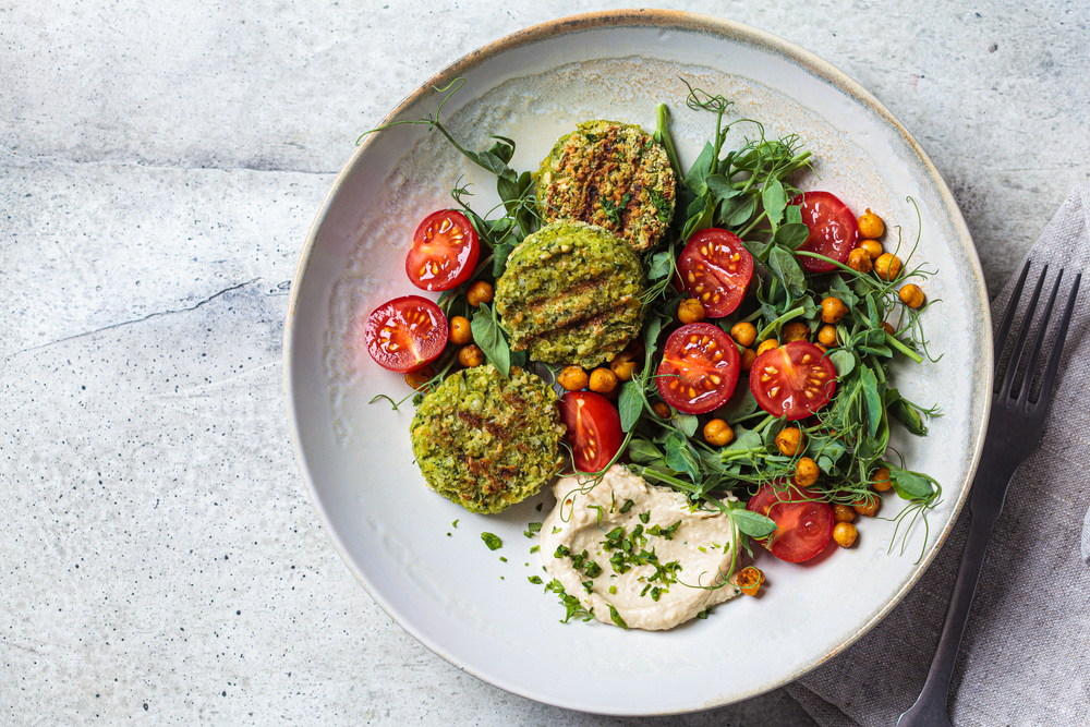 Falafel salad with tomatoes, hummus and pea sprouts in a gray bowl. Plant based food concept.