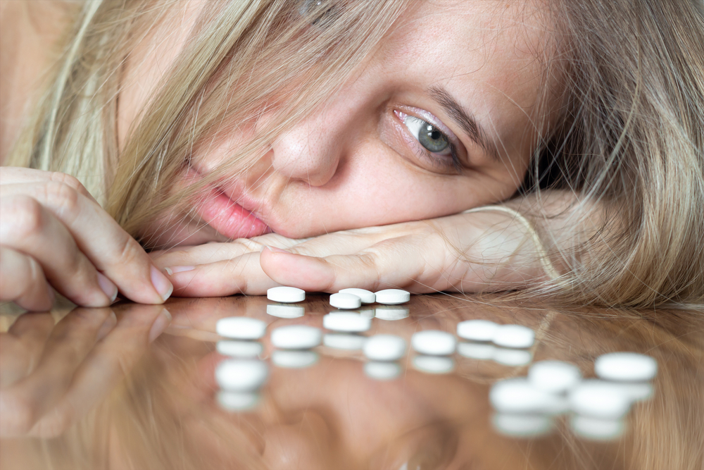 A young caucasian beautiful upset blonde woman puts her head on the table and looks at the antidepressants. Despair, apathy, depression, frustration, exhaustion, thoughts of suicide, mental disorder
