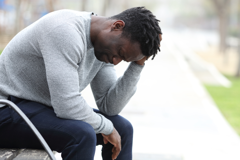 Profile of a sad black man complaining alone sitting on a bench in a park
