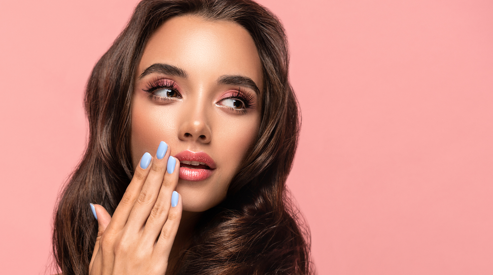 Beautiful woman showing blue manicure nails . Makeup and cosmetics. Brunette girl with long and shiny curly hair
