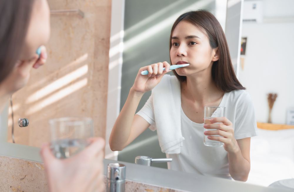 Morning Hygiene. Portrait Of Attractive Young Lady Brushing Teeth Near Mirror, Happy Beautiful Woman Smiling To Her Reflection While Standing In Bathroom With Toothbrush In Hand, Selective Focus
