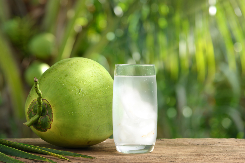 Glass of coconut juice with blurred coconut tree background.