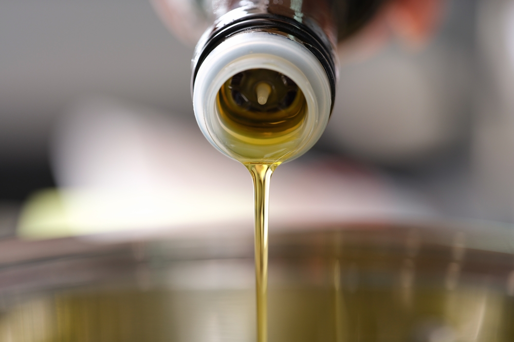 Clear olive oil is poured from dispenser bottle into saucepan closeup
