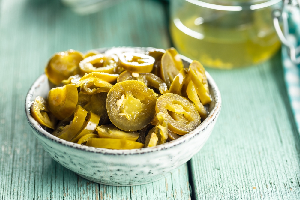 Pickled sliced jalapeno. Green jalapeno peppers in bowl on green table.
