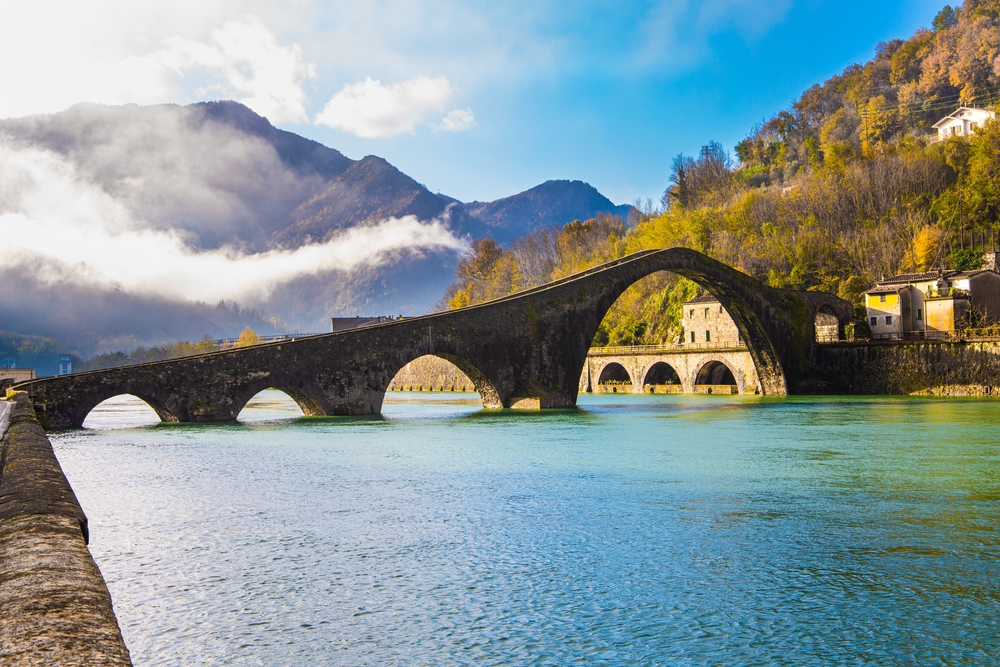 Italy, province of Lucca. Fancy Medieval Bridge - Devil's Bridge crosses the Serchio River. The green emerald cold water of the river reflects the ancient asymmetrical arches of the bridge
