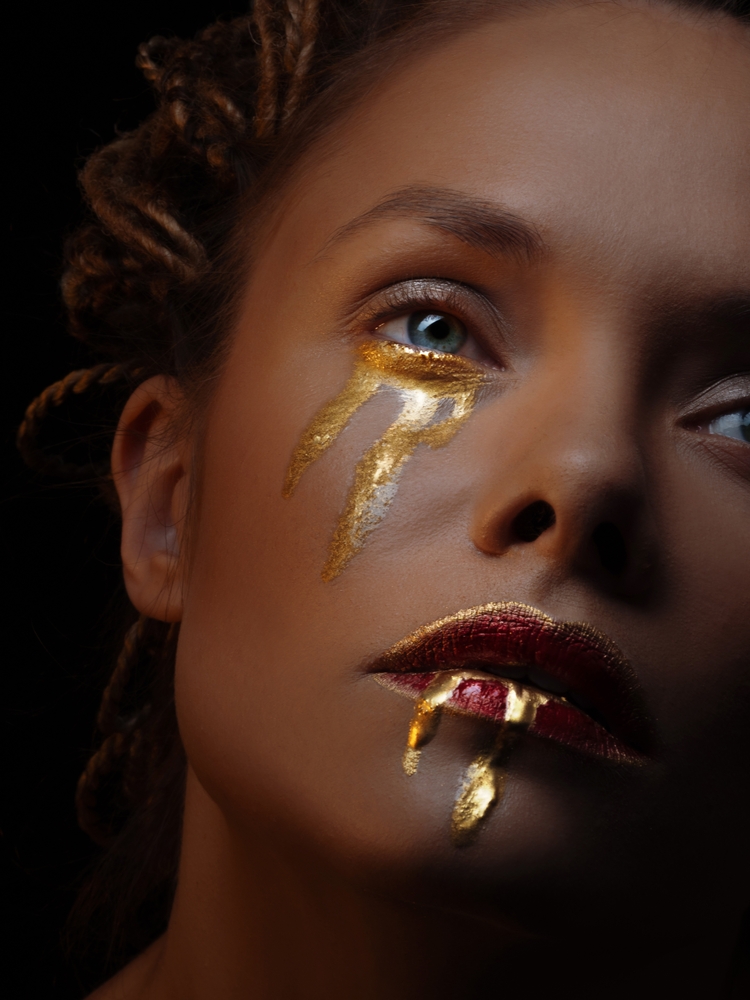 Mysterious mystical heroine with golden drops on her face, golden tears and blood, fantasy art. Portrait of a beautiful elegant woman in mystical art makeup