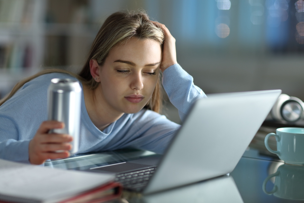Asleep student trying to study with a laptop holding energy drink in the night at home
