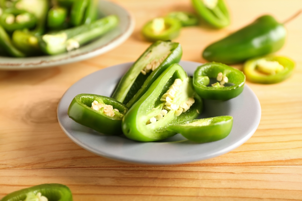 Plate with cut green jalapeno peppers on wooden background, closeup