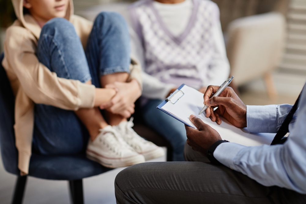 Close up of African-American psychologist taking notes on clipboard in therapy session for children
