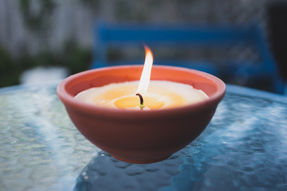 citronella candle with flame outdoor on cafe table setting at dusk for protection against mosquitoes during summer nights