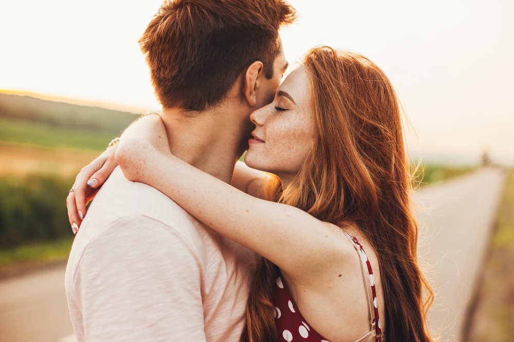 Close-up portrait of a caucasian young loving couple embracing while standing on a roadside. Couple embracing road travel. Sunset scene.
