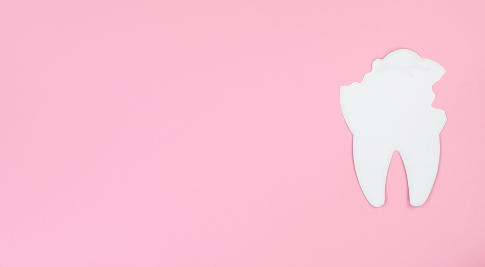 White paper tooth with caries on a pink background, space for text

