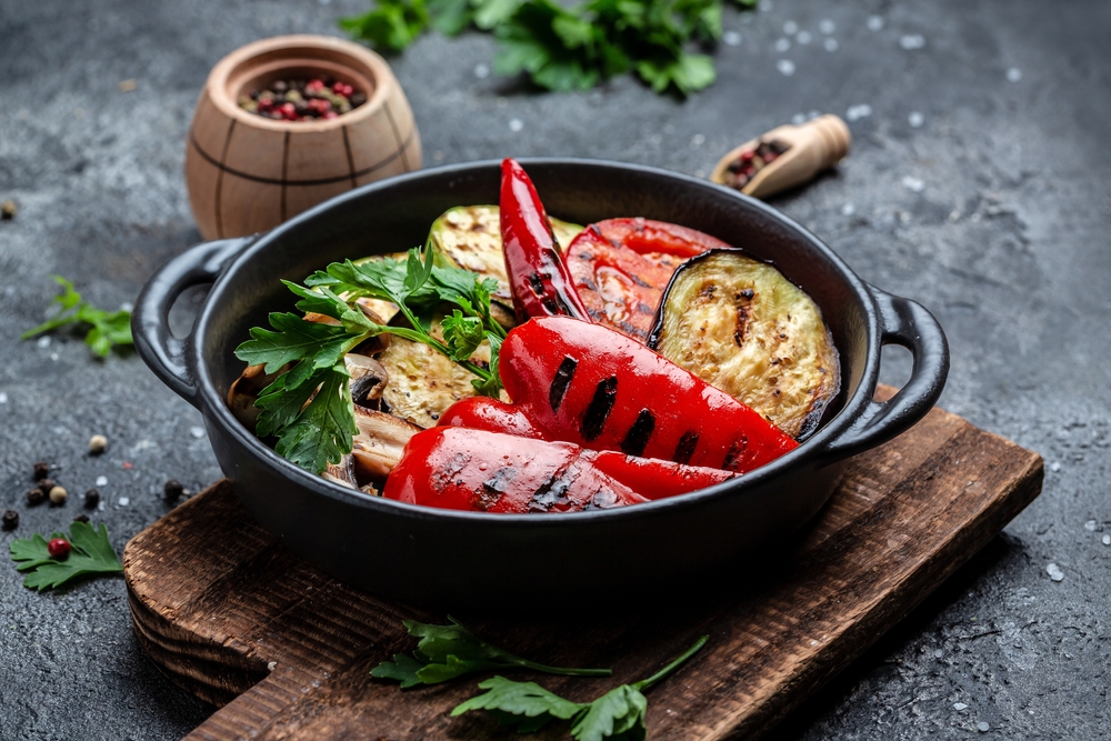 Grilled vegetables colorful bell pepper, zucchini, eggplant with herbs in a cast iron grilling pan over stone, concrete background. Restaurant menu, dieting, cookbook recipe top view.
