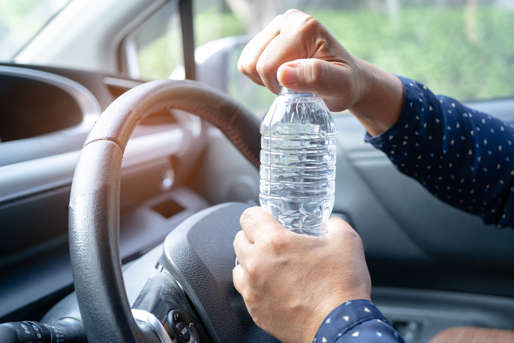 Asian woman driver holding bottle for drink water while driving a car. Plastic hot water bottle cause fire.
