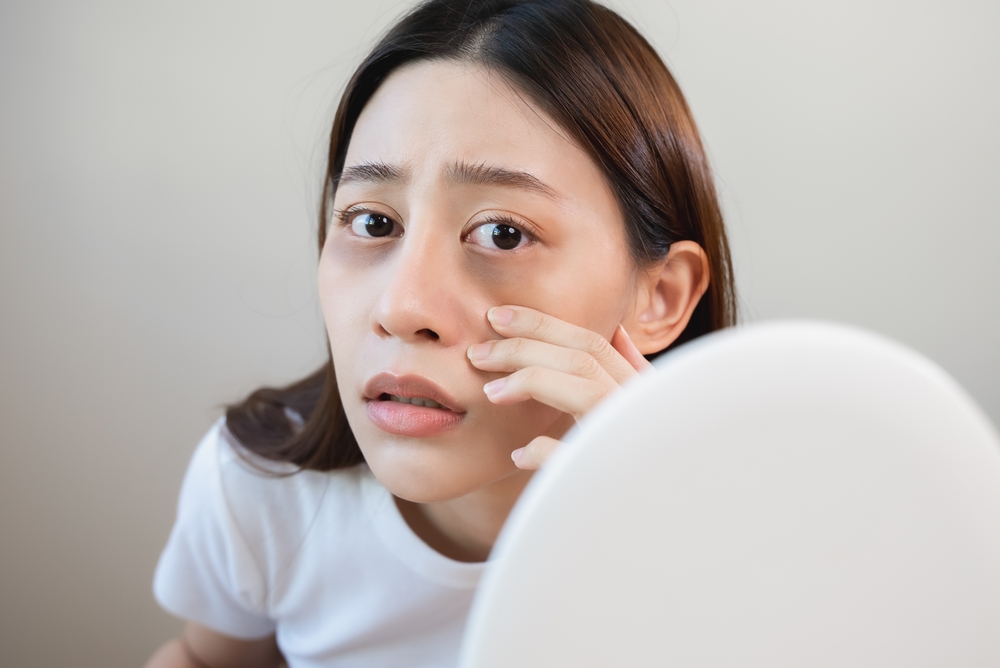 Sleepless Asian woman looking her face in the mirror and worry about dark circles under eyes
