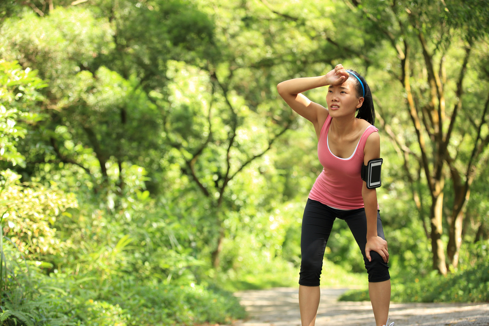 tired female runner taking a rest after running hard in countryside road. sweaty athlete after marathon training in country road.