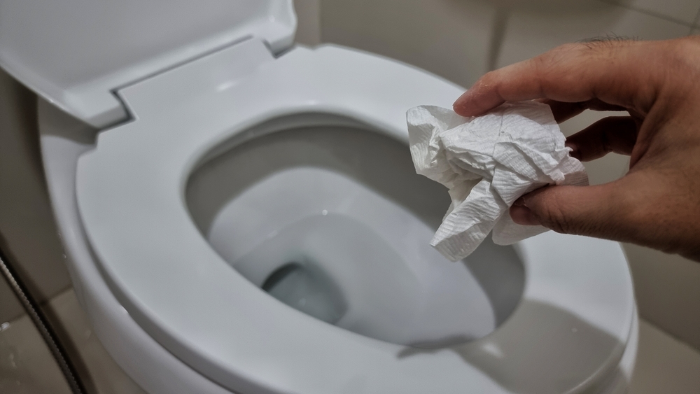 Hand throwing tissue paper directly in the toilet bowl.

