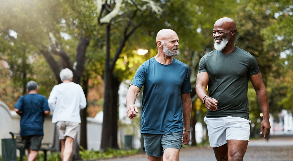 Fitness, exercise and men walking together at community park while talking and doing cardio training outdoor in nature. Diversity, friends and senior man and accountability partner on a wellness walk