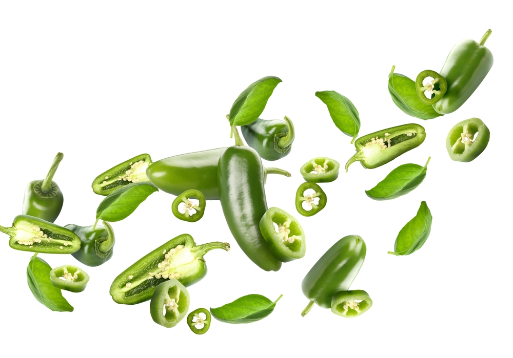Flying green jalapeno peppers and fresh basil leaves on white background