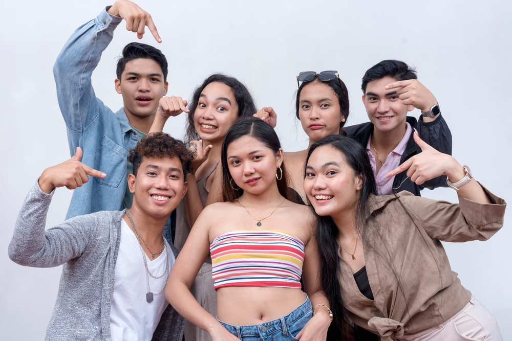 A group of seven happy and young people in their late teens to early 20s pointing to their friend in the middle. Presentation and advertising concept. Isolated on a white backdrop.