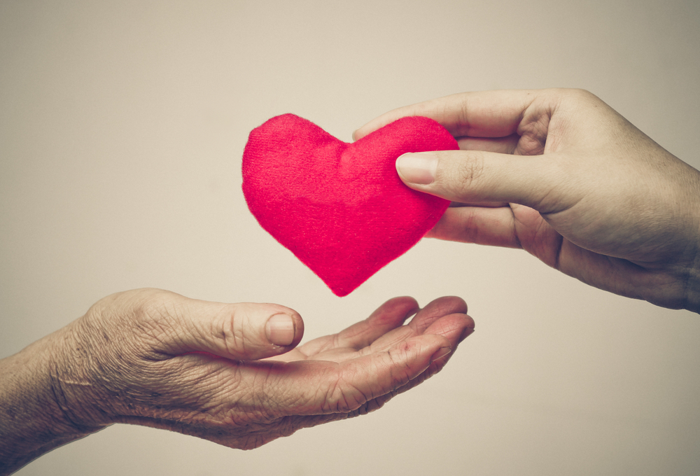take care of old mother - young female hand giving a red heart to old hand of a mother - happy mother's day
