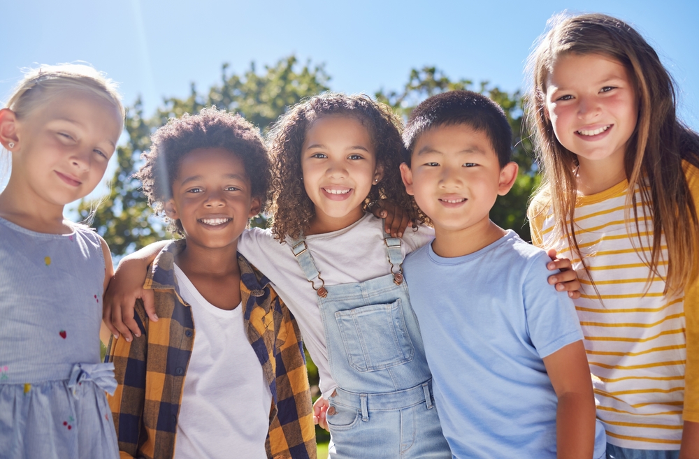 Friendship, kids and portrait of friends in a park playing together outdoor in nature. Happiness, diversity and children with a smile standing, embracing and bonding in a outside garden or playground
