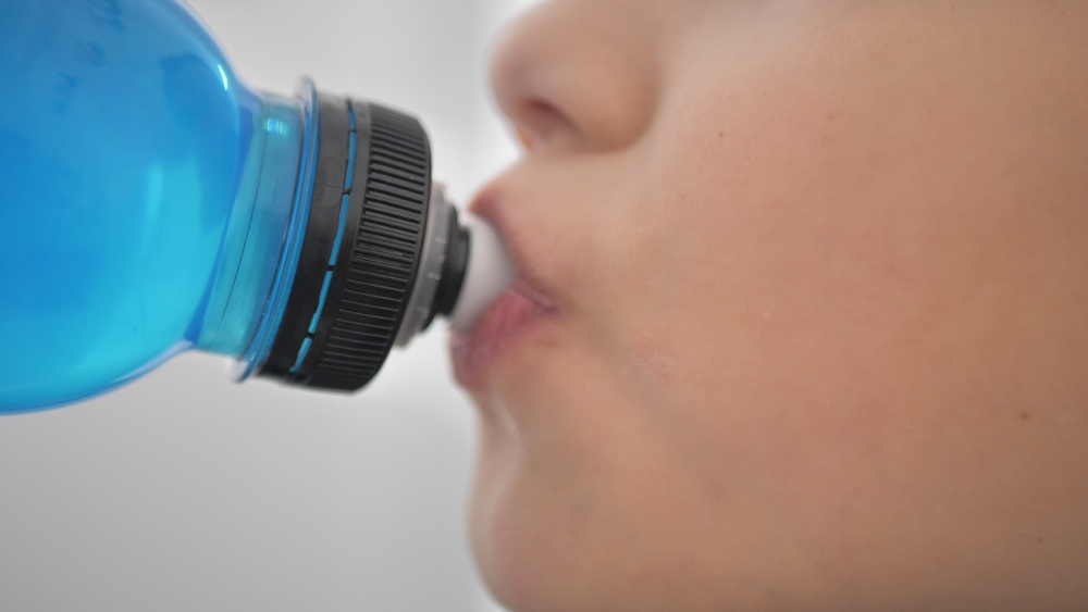 Taking a break. Side view of sporty teenager drinking blue energy drink. Youth and sports