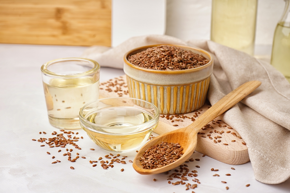 Bowl, glass with flax oil and spoon of seeds on white background