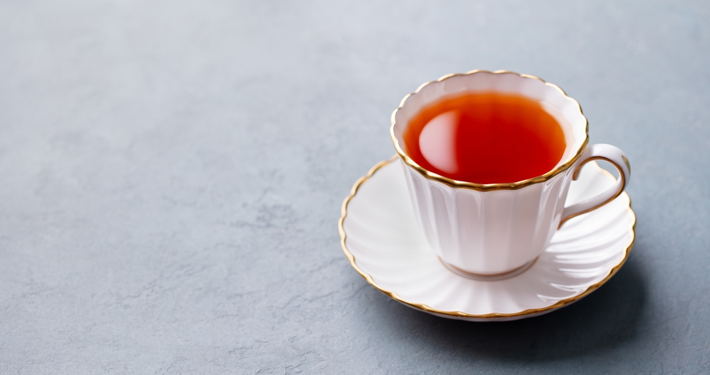 Tea in white cup with gold rim. Grey background. Copy space.