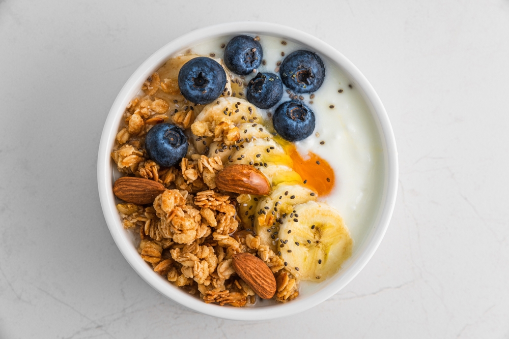 Healthy breakfast. Bowl of greek yogurt with oat granola, fruits, nuts, honey and chia seeds. Top view. Diet food