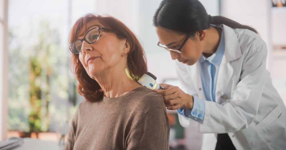 Portrait of a Young Asian Dermatologist Using a Medical Magnifying Glass to Inspect any Damages on the Skin of a Senior Patient During a Health Check Visit to a Clinic. Doctor Working in Hospital