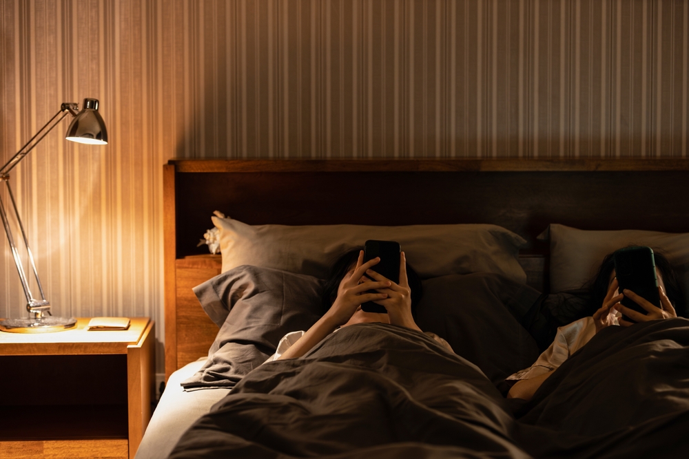 Asian female with nomophobia,excessive use of cell phone,addicted to social media,lying on bed looking at mobile phone screen in bedroom at night before bedtime,smartphone syndrome,Nomophobia concept
