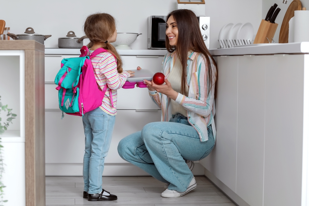 Mother giving school lunch to her little daughter in kitchen