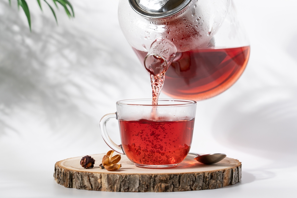 Hot tea is pouring from glass teapot into cup. Hibiscus red tea in glass cup close-up view