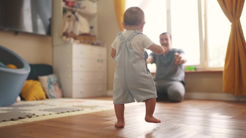 baby first steps. baby goes her father at window learns to walk to take first steps. happy family kid dream concept. dad calls son baby first steps indoors. happy family lifestyle indoors concept
