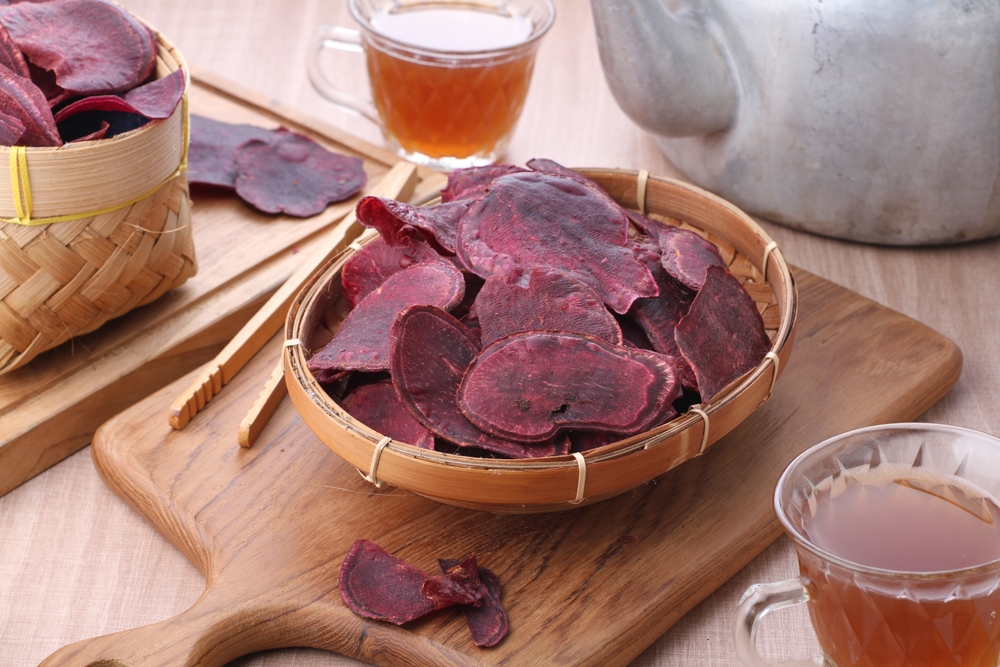 Plate with slices of fried purple potatoes, lemon and sauce on light background
