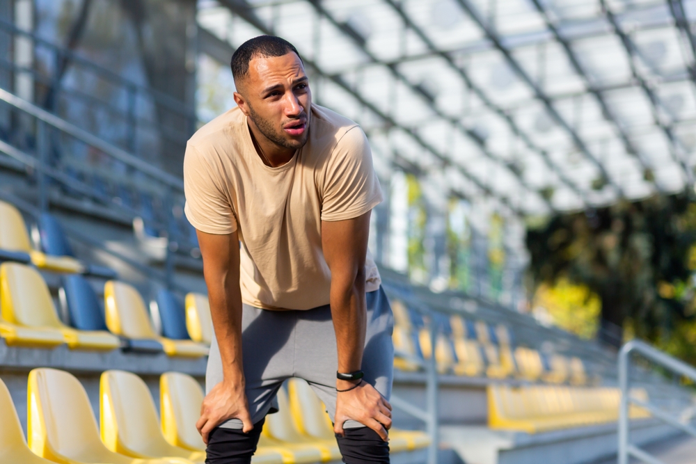 Tired hispanic athlete bent over and breathing after jogging, man doing sports on sunny day with active exercises and fitness, athlete resting after jogging.