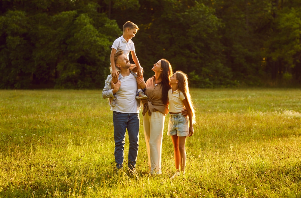 Happy family strolling in nature all together. Happy, joyful mother, father and little children walking on green grass in a beautiful park on a sunny summer evening

