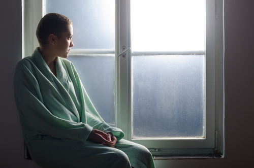 Young cancer patient sitting in front of hospital window.
