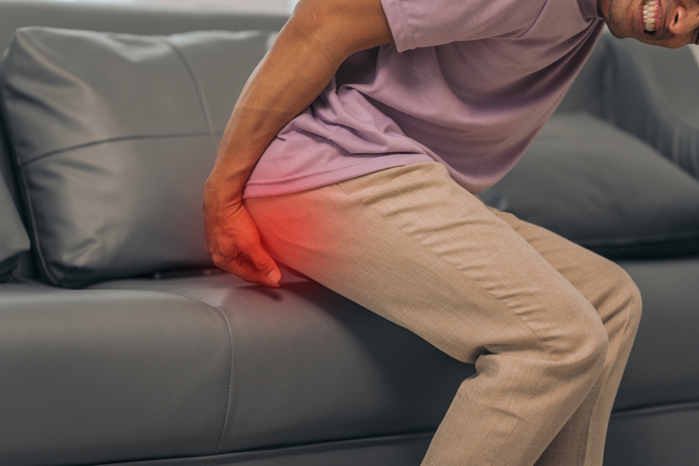 Middle-aged Asian Indian man with butt pain, hemorrhoids, colon pain, sitting on a sofa.
