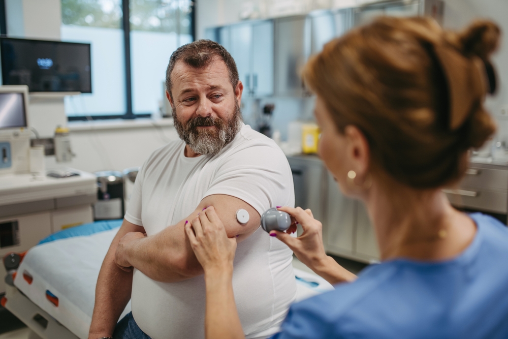 Doctor applying a continuous glucose monitor sensor on patient's arm. Obese, overweight man is at risk of developing type 2 diabetes. Concept of health risks of overwight and obesity.

