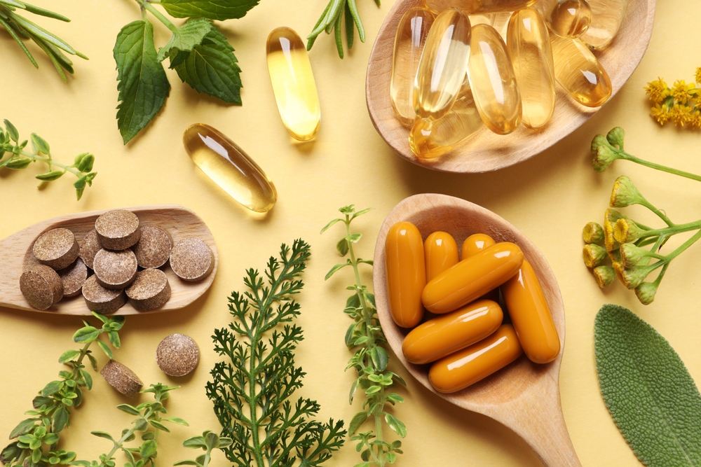 Different pills and herbs on pale orange background, flat lay. Dietary supplements

