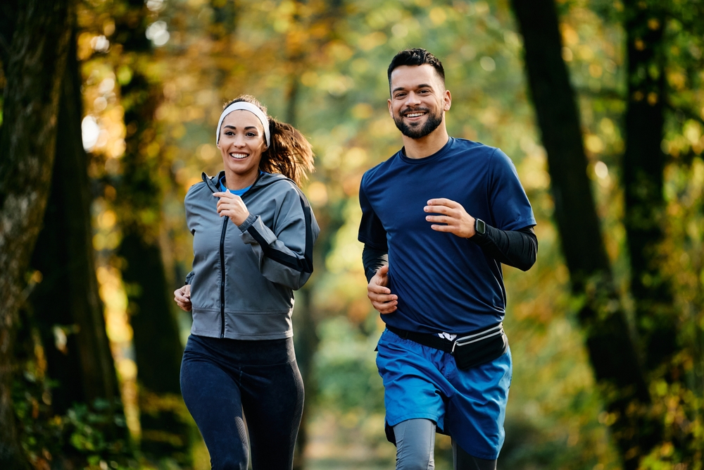Happy athletic couple jogging during autumn day in the park.