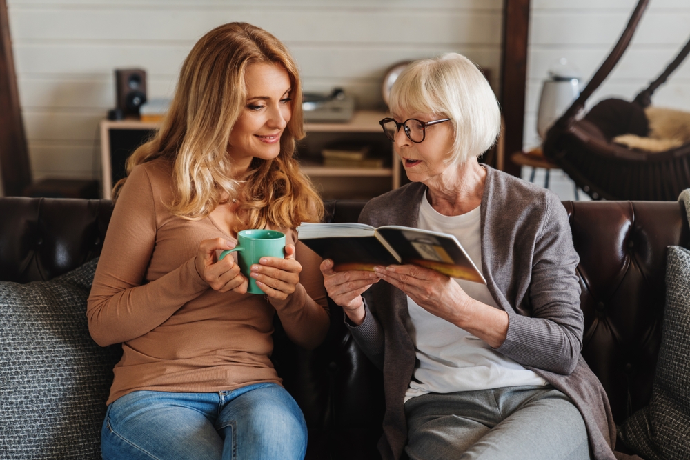 Senior mother and daughter looking photo book, resting at home. Memories, childhood, family time together. Grandchildren visiting grandparents
