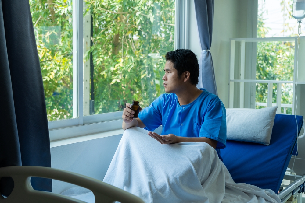 Young Asian patient on a hospital bed with a sad look at a hospital examining a patient on a bed while wearing a blue hospital gown.