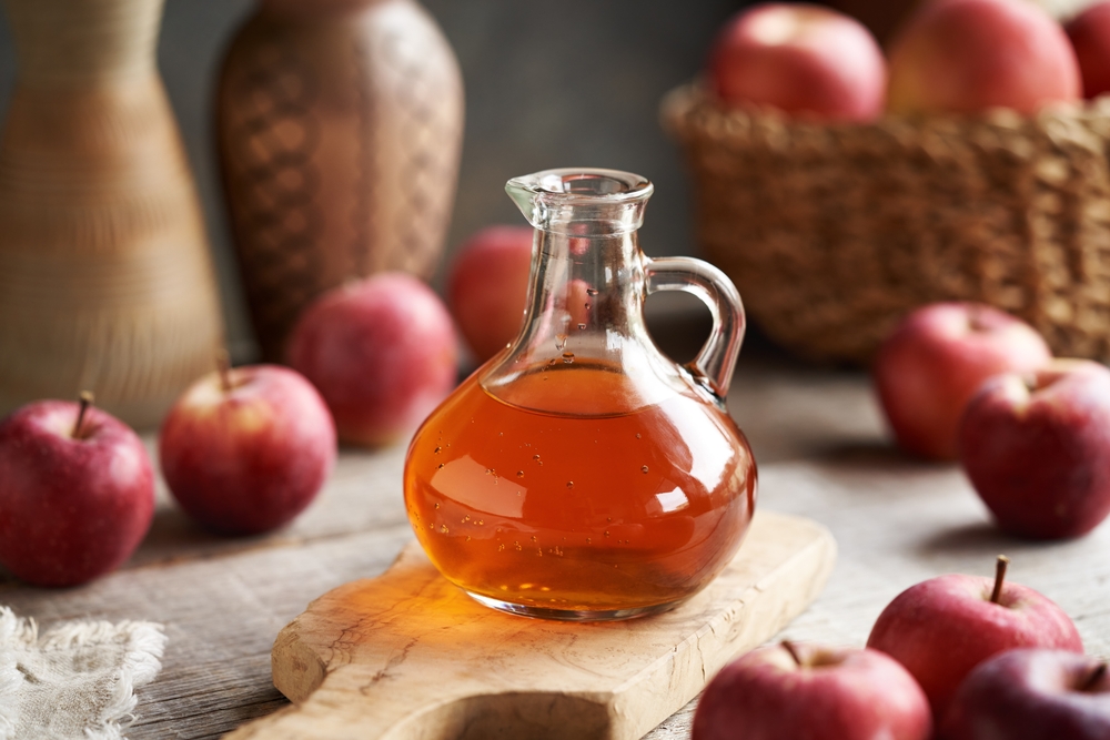 A glass jug of apple cider vinegar with fresh fruit on a table