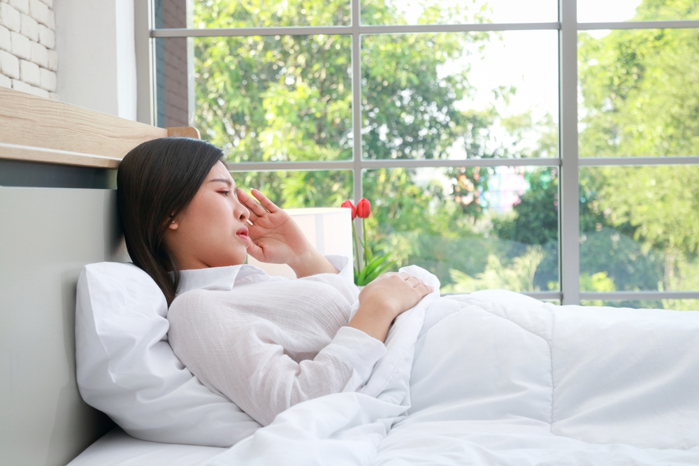 Asian woman is sick and has a headache. She is resting in bed. Health concept. Flu caused by a virus