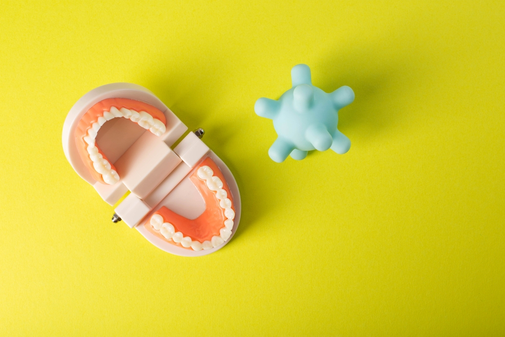 A model of a virus and bacteria near a mock-up of a dental jaw on a yellow background. The concept of oral dysbiosis, pathogenic microorganisms and microbes that destroy tooth enamel and caries.